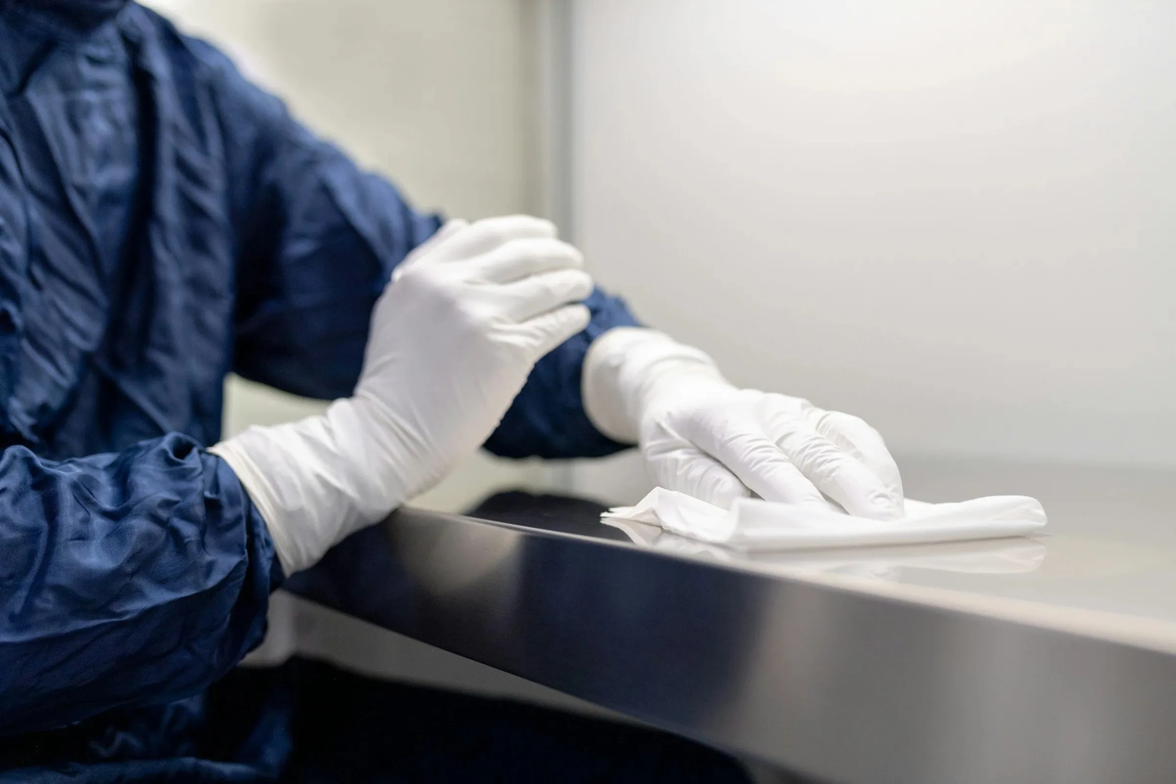 Cleaner in protective clothing wiping a surface with white gloves